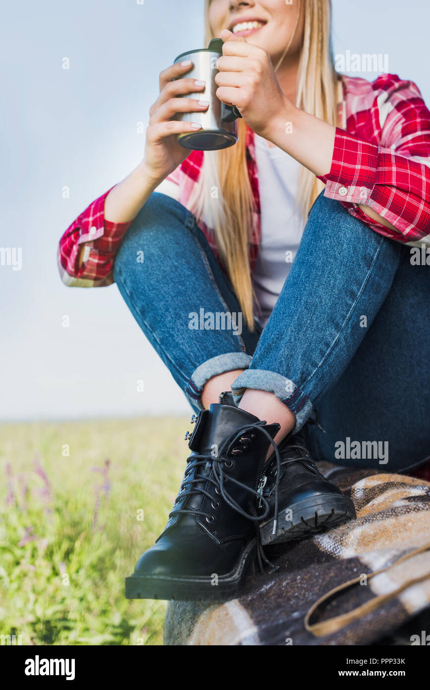 cropped image of young woman sitting on car trunk with coffee cup in rural field Stock Photo