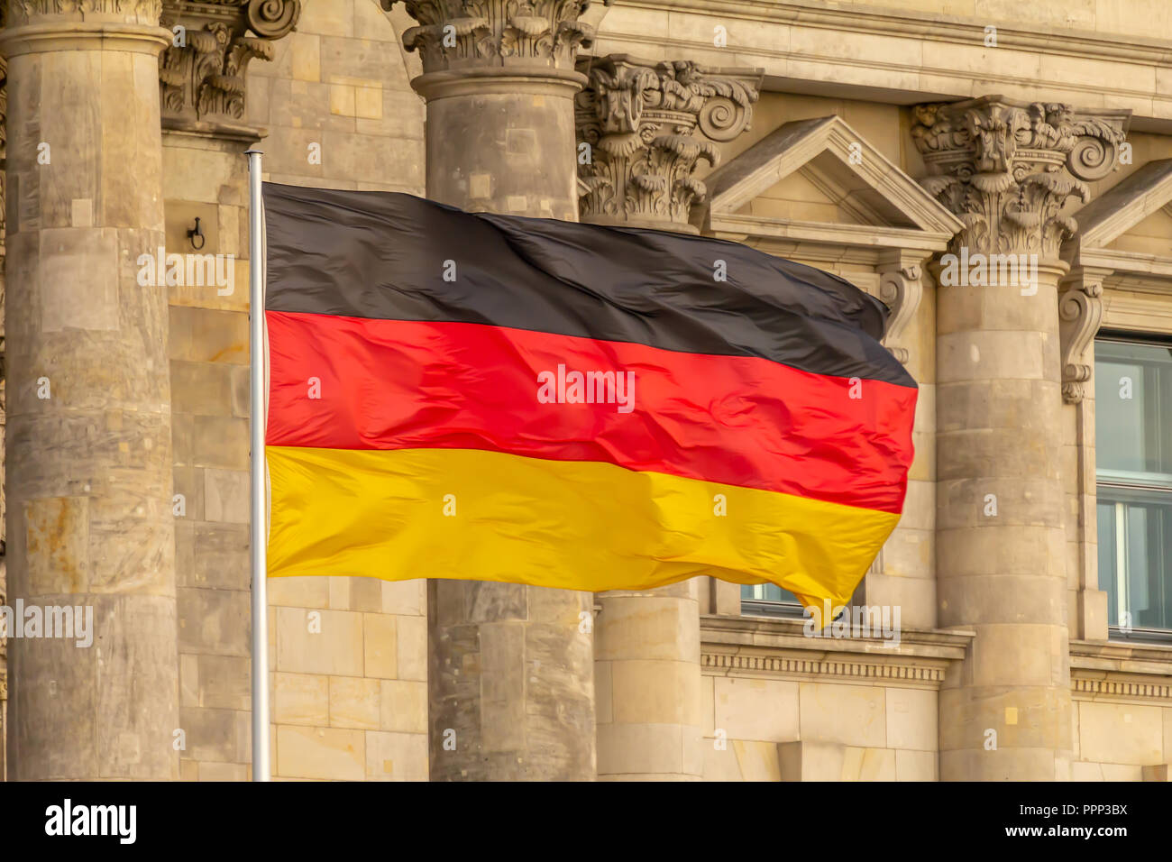 Federal Republic of Germany, German national flag waving in front of the Parliament building columns Stock Photo