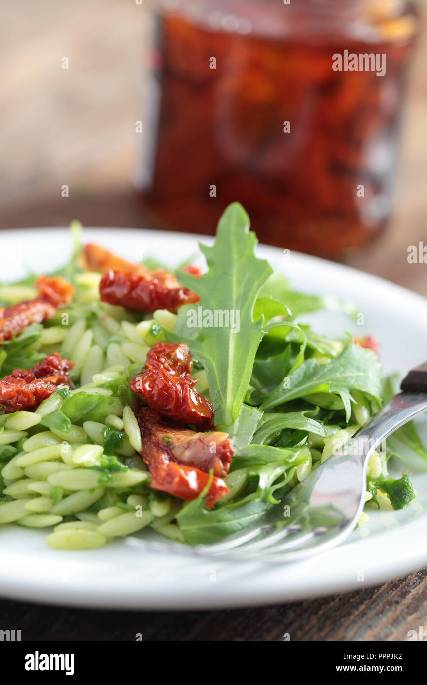 Salad with orzo pasta, rocket, pesto sauce, and sun-dried tomatoes Stock Photo