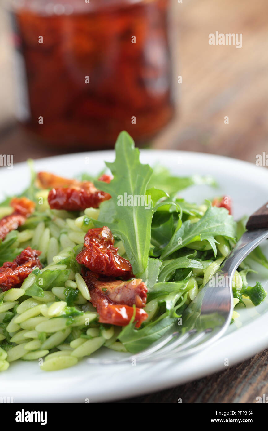 Salad with orzo pasta, rocket, pesto sauce, and sun-dried tomatoes Stock Photo