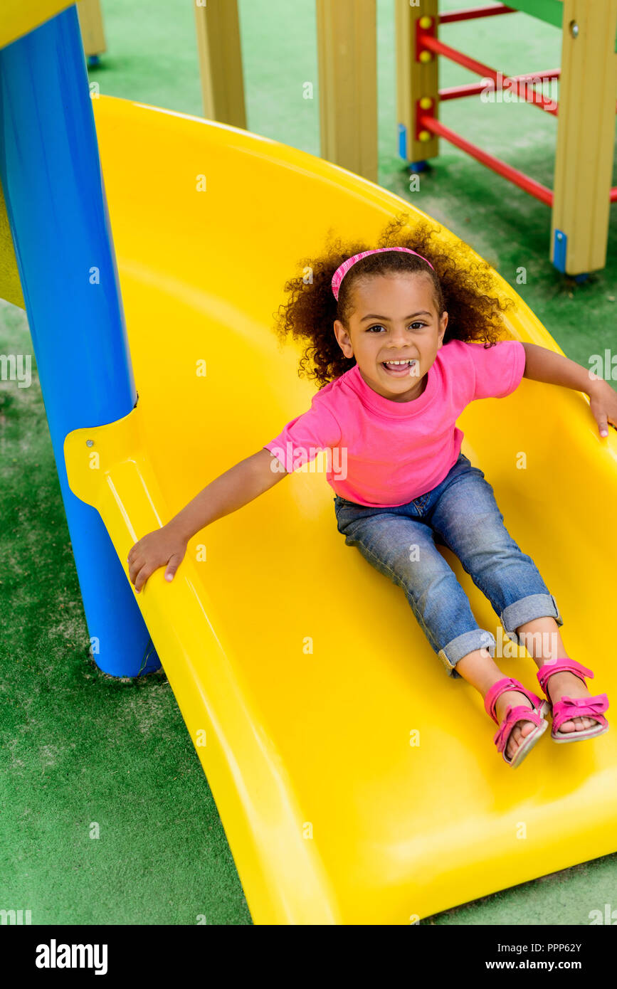 smiling curly african american little kid sliding down from hill at