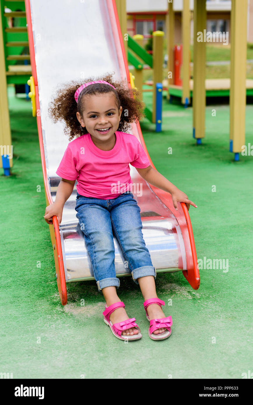 smiling curly african american little kid sliding down from hill at