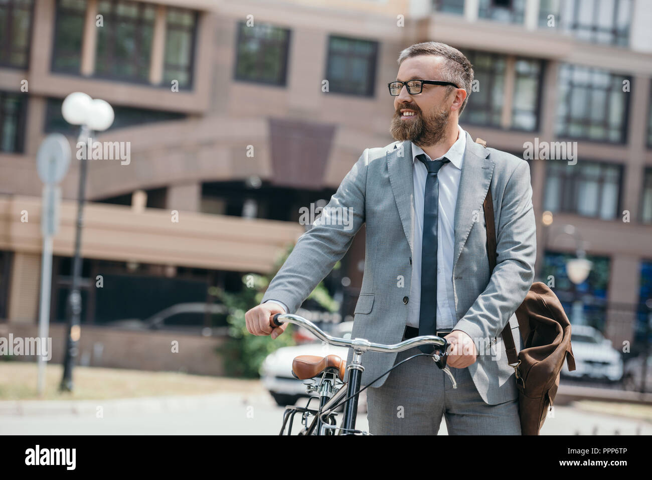 handsome businessman walking with bicycle on street in city and looking away Stock Photo