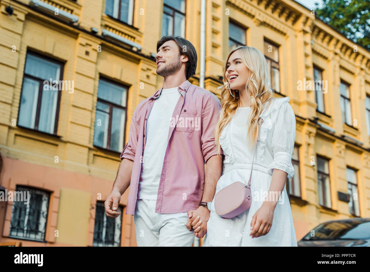 young couple holding hands while walking on city street together Stock ...