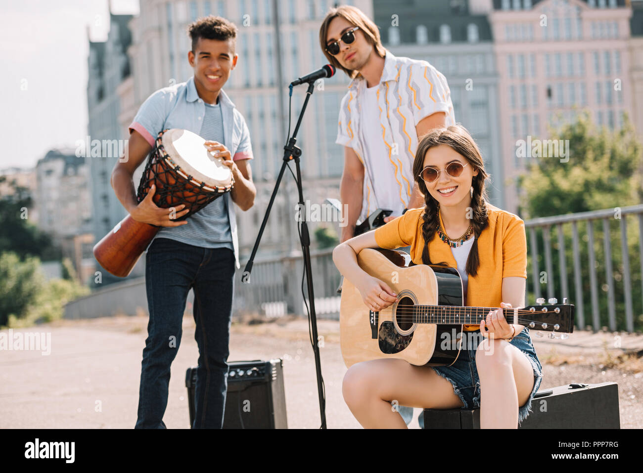 Multiracial young people performing on guitars and djembe on street Stock Photo