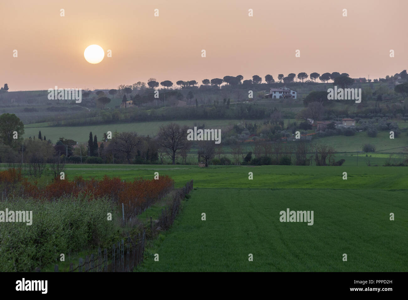 Sunset with sand suspended in the atmosphere, coluring the sky red, over some green fields and hills Stock Photo