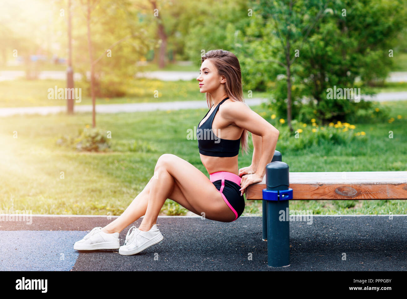 Young sporty woman doing triceps dip exercise on city street bench. Stock Photo