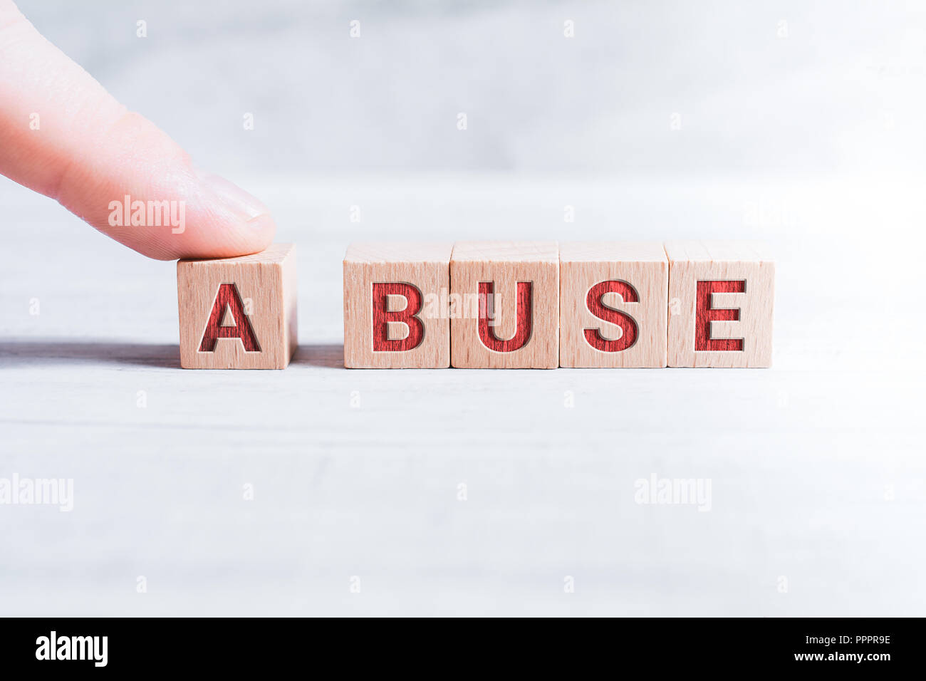 The Word Abuse Formed By Wooden Blocks And Arranged By A Male Finger On A White Table Stock Photo