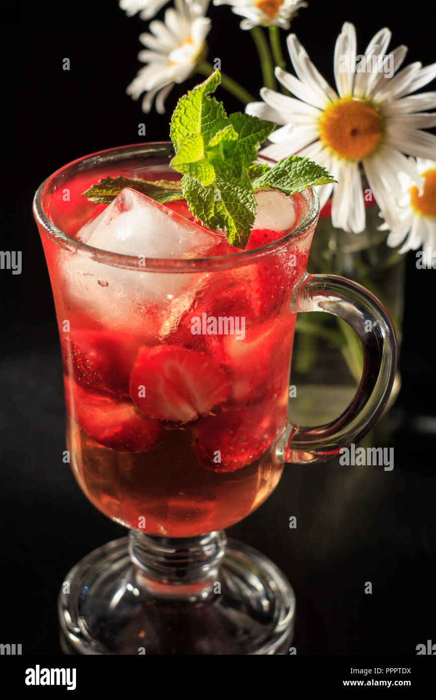 Carbonated lemonade with strawberry slices and mint with flowers of chamomile on the black background. Cold beverage for hot summer day Stock Photo