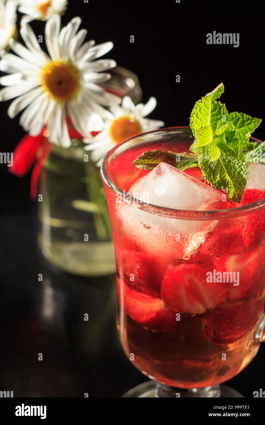 Carbonated lemonade with strawberry slices and mint with flowers of chamomile on the black background. Cold beverage for hot summer day Stock Photo