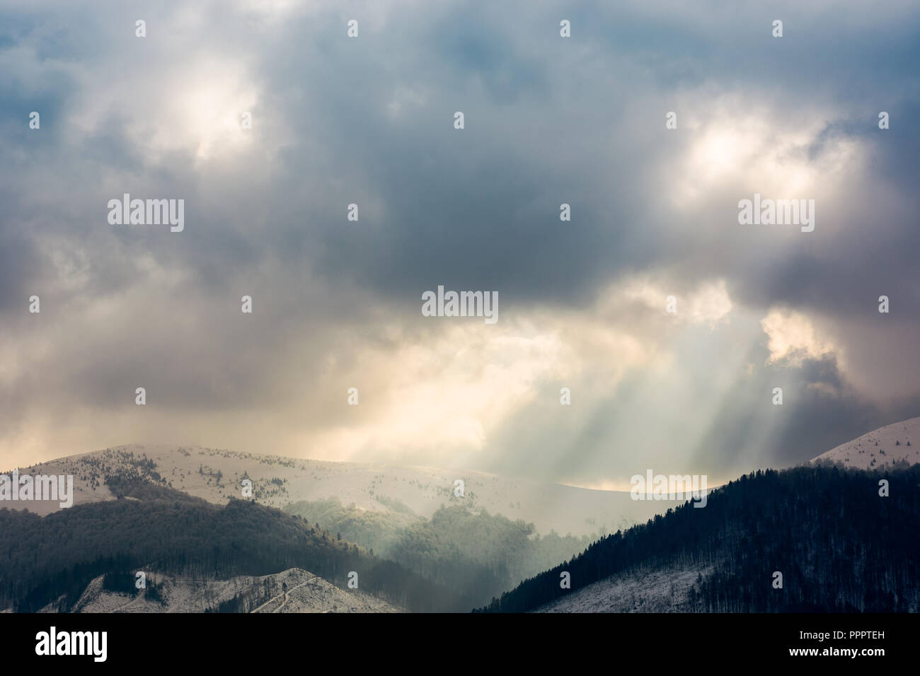 overcast sky with light beams over the ridge. dramatic winter scenery in mountains with snowy tops Stock Photo