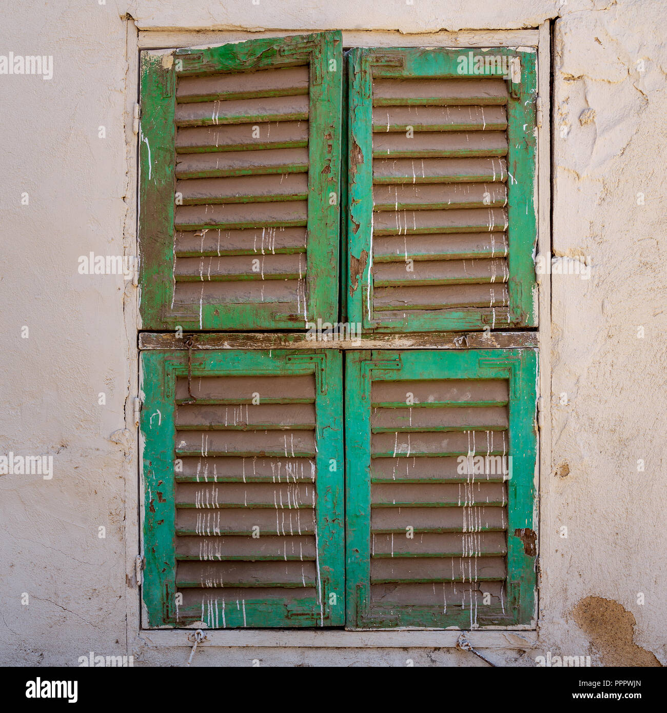 Old grunge window with closed green shutters on dirty bricks stone wall