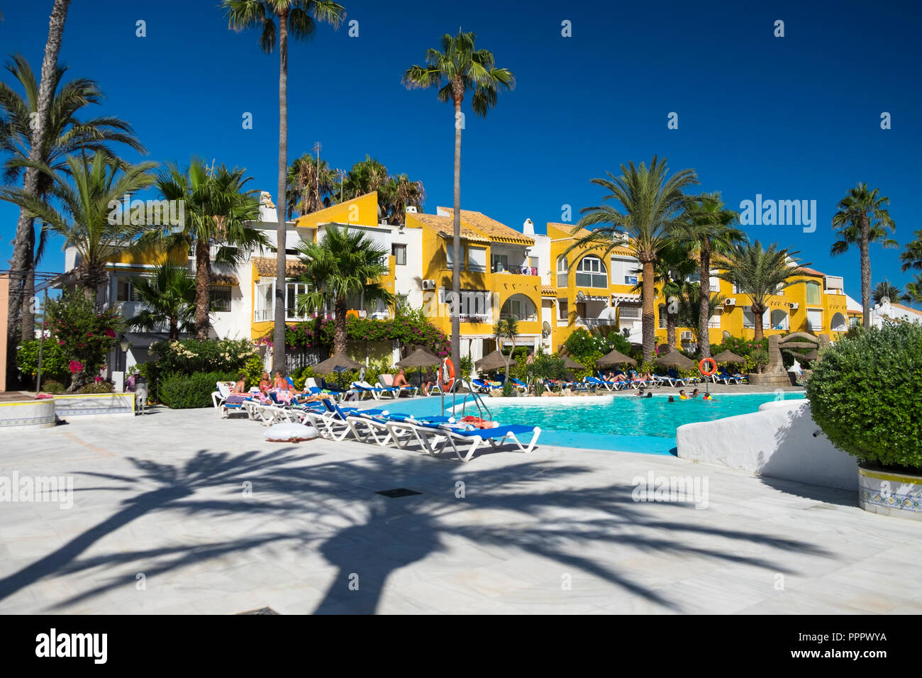 Apartments los mangos, palm trees, people by the swimming pool, blue sky and hot weather, roquetas de mar, almeria, spain Stock Photo