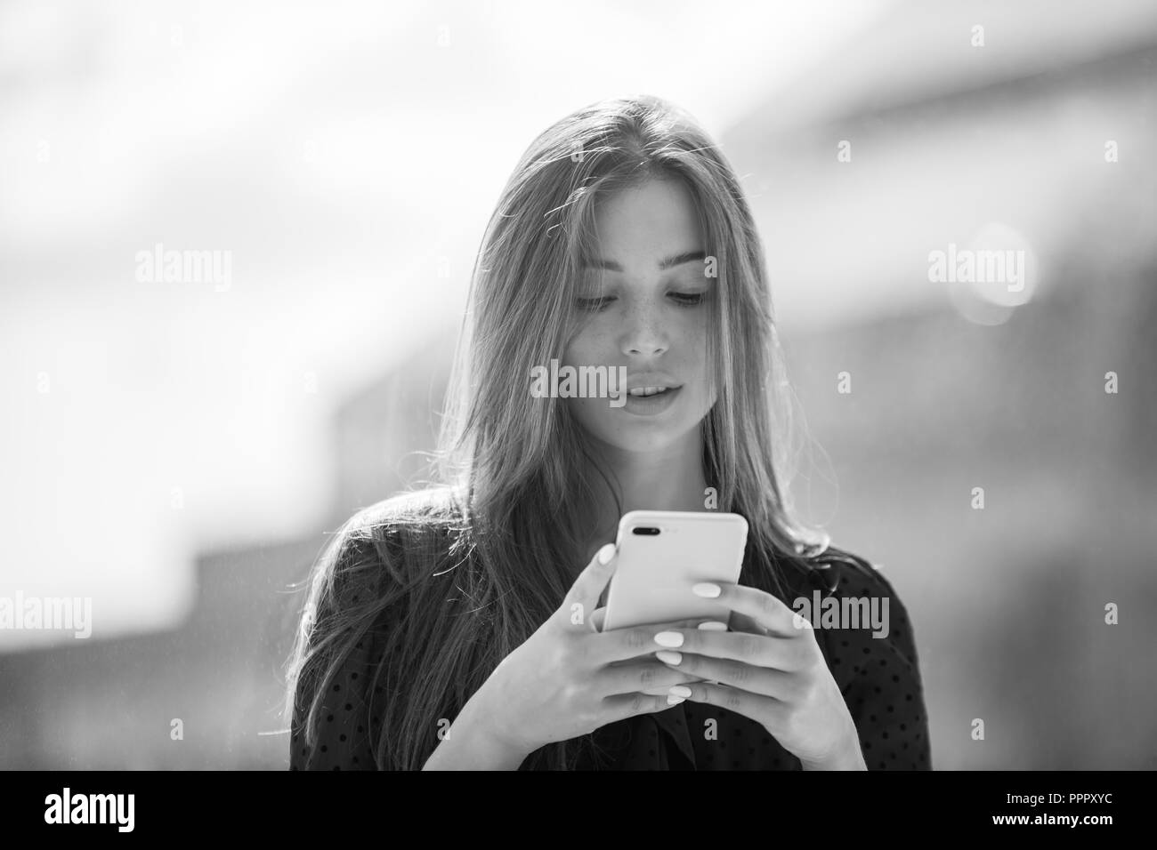 Attractive woman is sitting on the windowsill and uses a smartphone. Stock Photo
