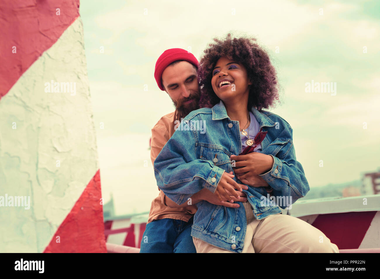 Cute young couple laughing while sitting on the roof together Stock Photo
