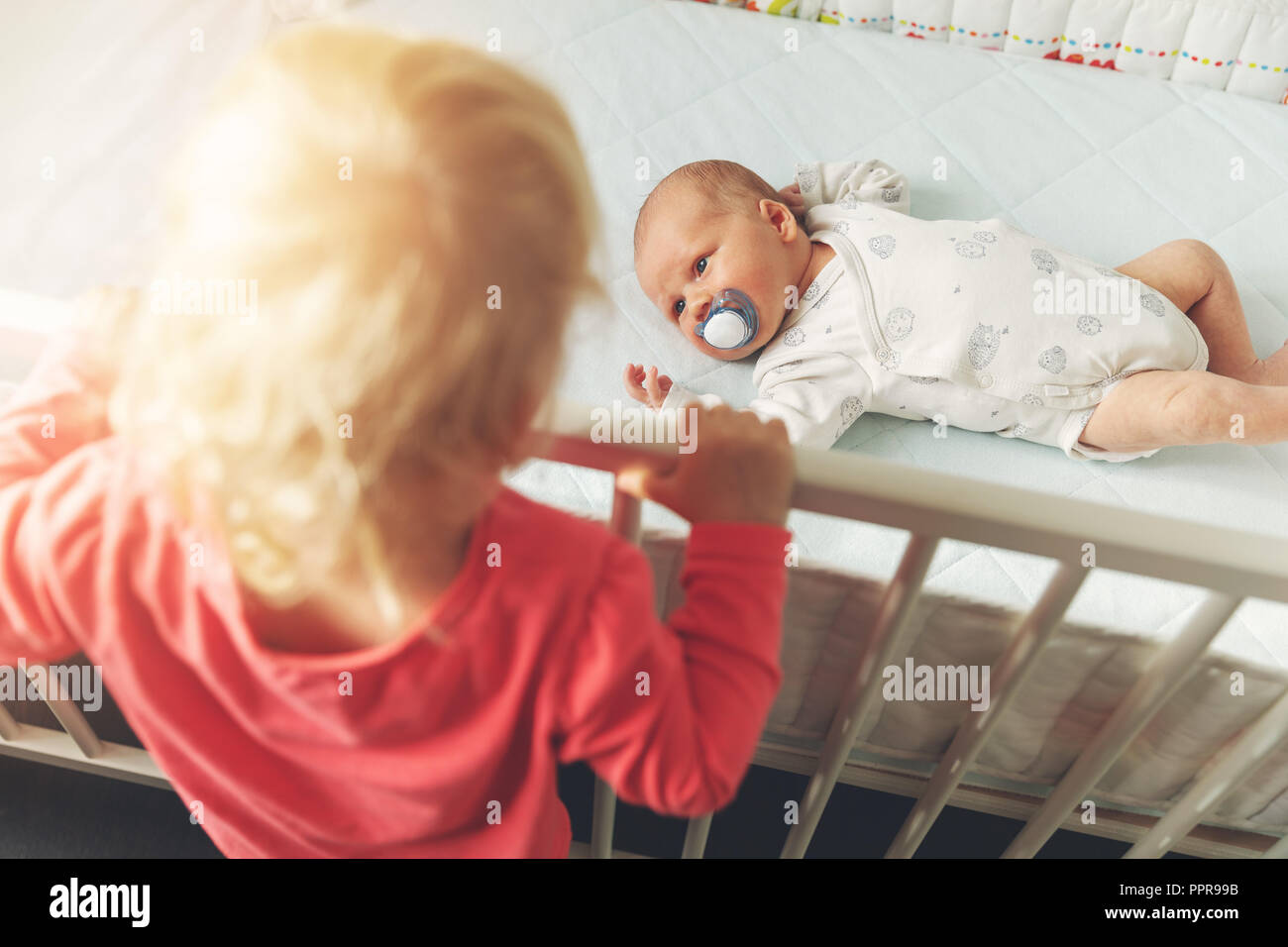 sister looking at newborn brother in cot Stock Photo