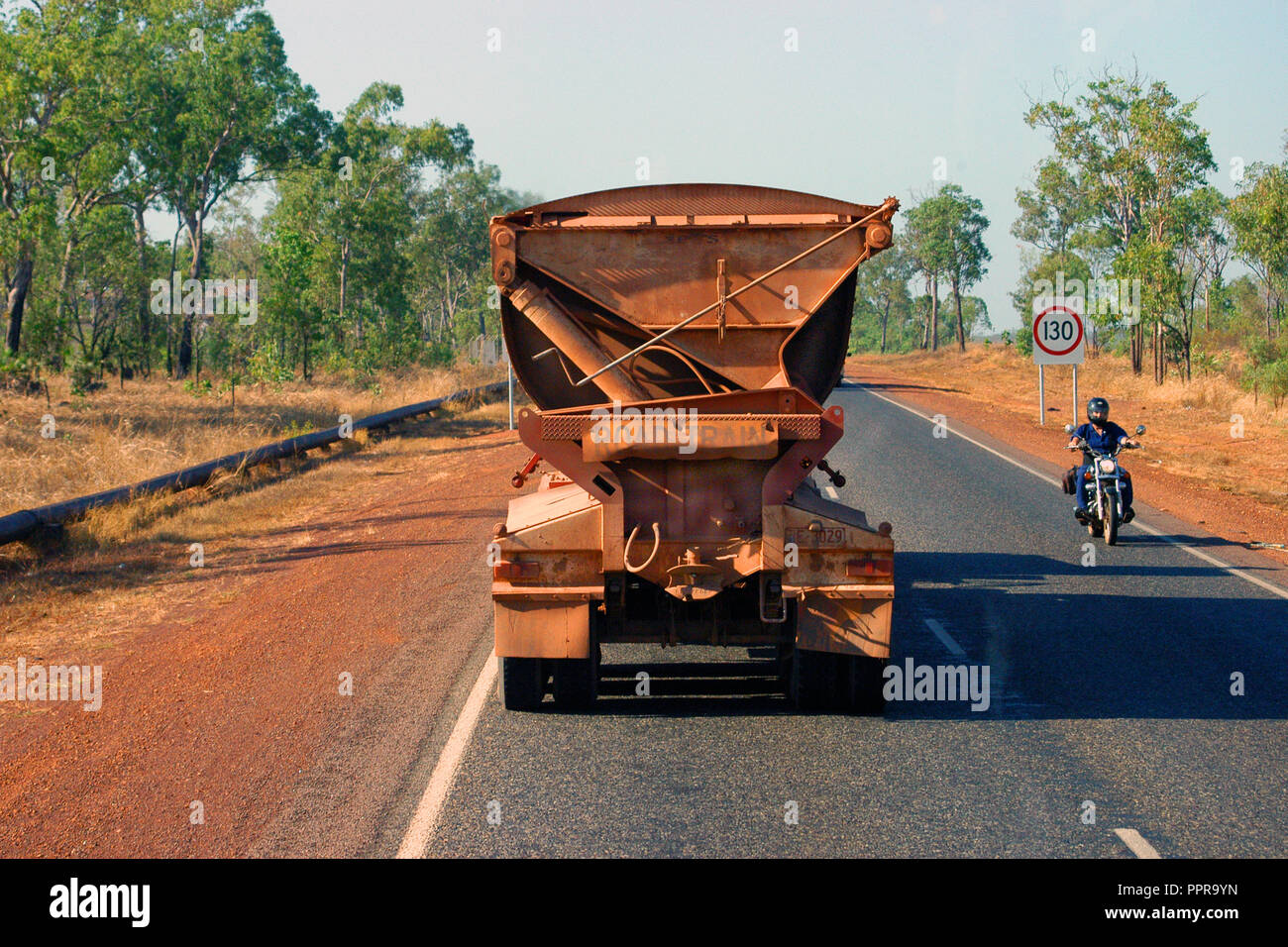 REAR VIEW OF A ROAD TRAIN ON THE STUART HIGHWAY, A MOTORBIKE RIDER TRAVELS IN THE OPPOSITE DIRECTION, NORTHERN TERRITORY, AUSTRALIA. Stock Photo