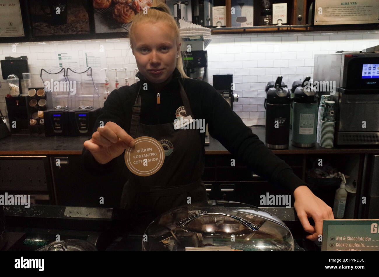 September 26, 2018 - Stockholm, Sweden: An employee of Expresso House shows a sign in Swedish language that means 'We Are a Cashless Coffee shop'. Sweden is the most cashless society on the planet, with 80% of all transactions in made with bank cards or mobile phone apps. *** FRANCE OUT / NO SALES TO FRENCH MEDIA *** Stock Photo