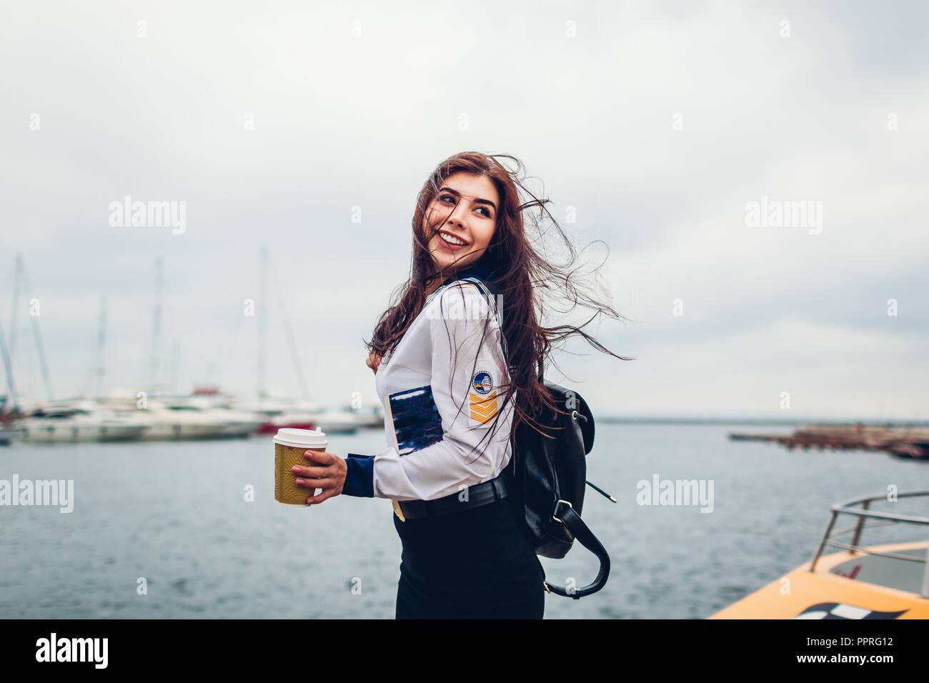 College woman student of Marine academy drinking coffee by sea wearing uniform. Girl walking in seaport of Odesa on pier Stock Photo