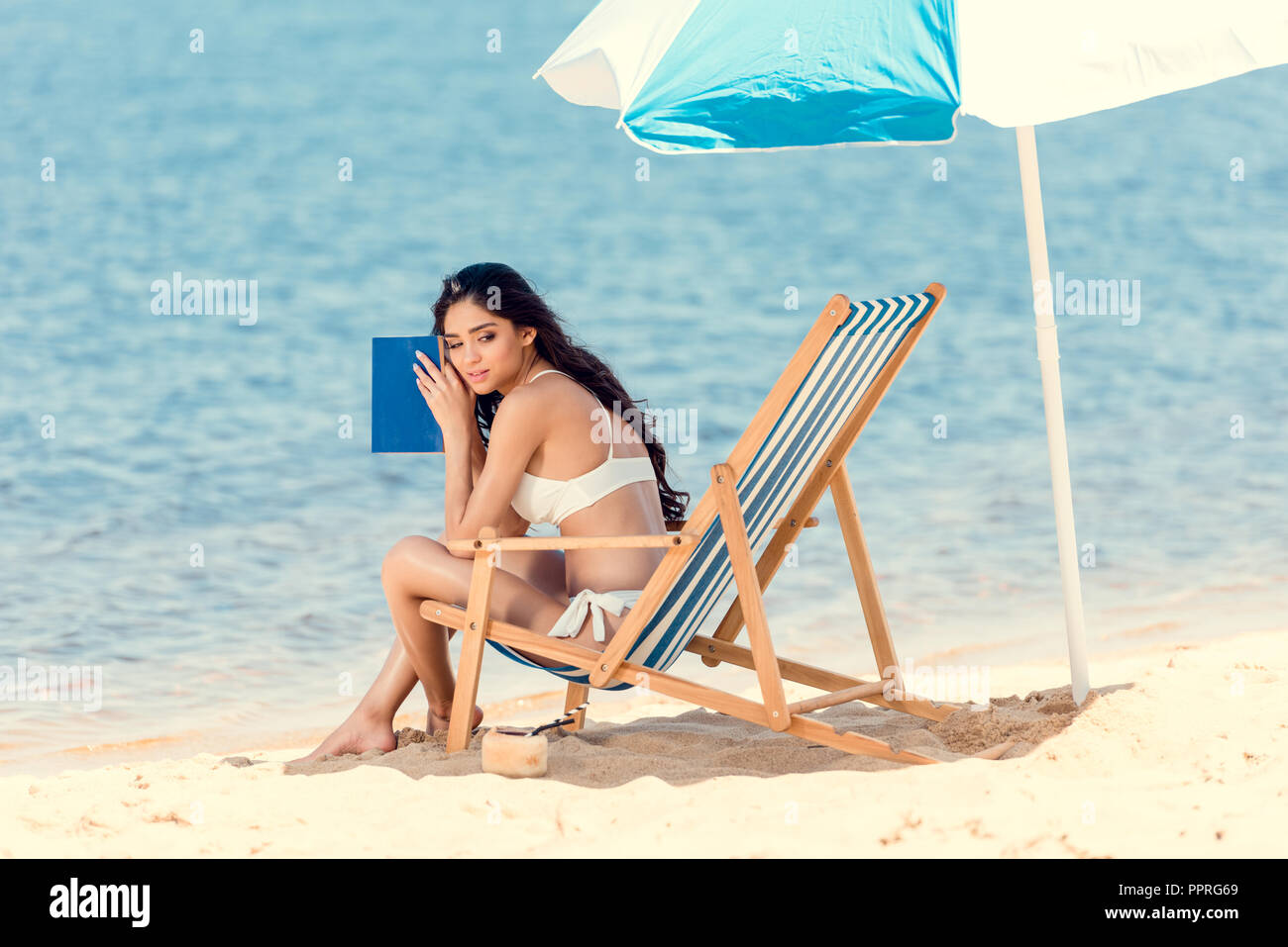 attractive girl in white bikini with book on beach chair near sea  attractive girl in white bikini with book on beach chair near sea