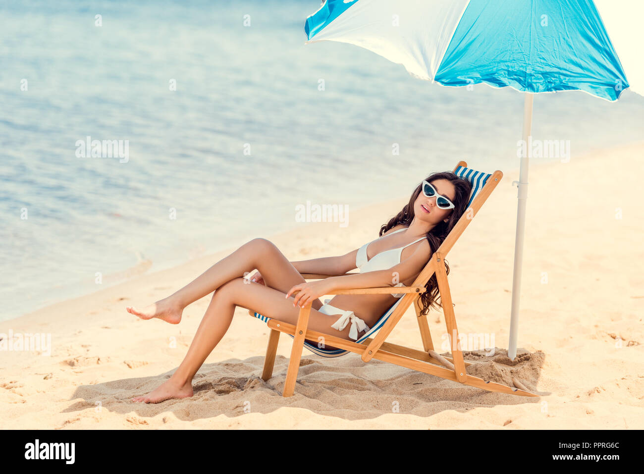 woman in sunglasses and bikini relaxing on beach chair under  woman in sunglasses and bikini relaxing on beach chair under
