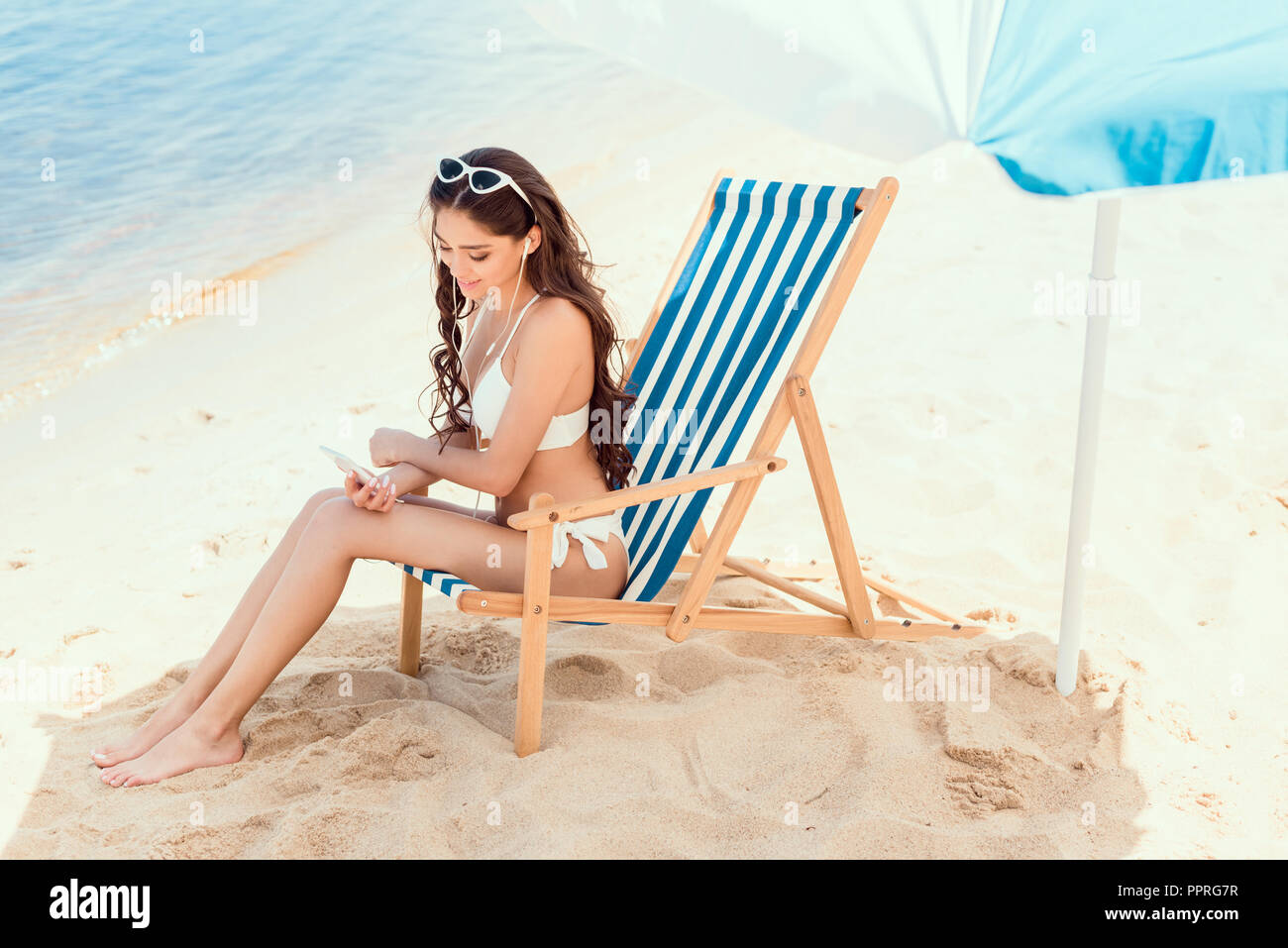 attractive woman using smartphone and resting on beach chair under  attractive woman using smartphone and resting on beach chair under