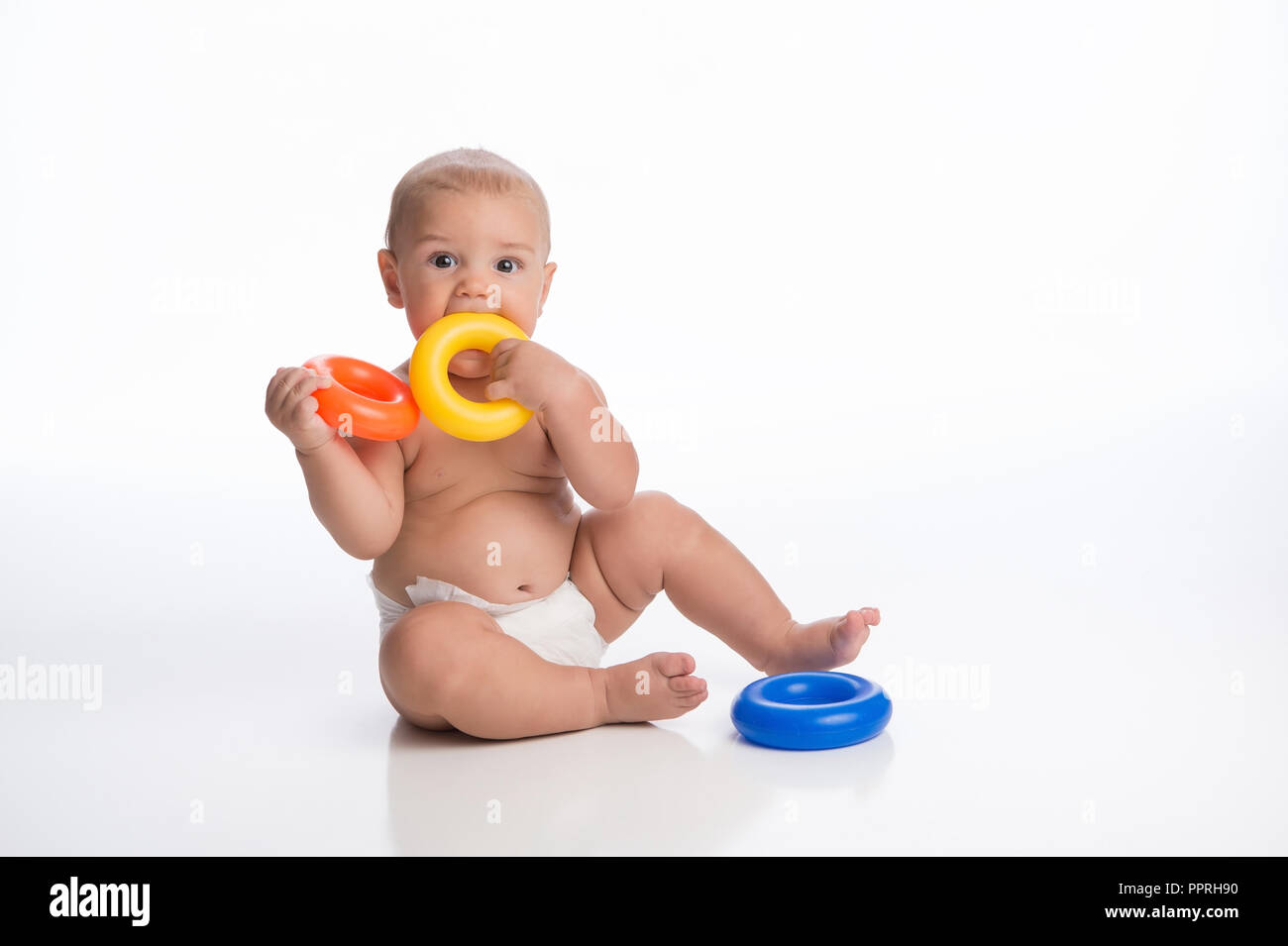 A seven month old baby boy, with a cute expression, putting a toy ring in his mouth. Shot in the studio on a white, seamless backdrop. Stock Photo