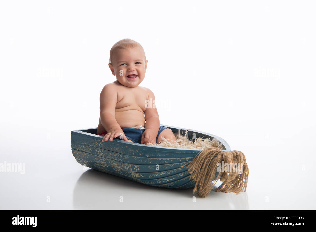 A smiling seven month old baby boy sitting in a rustic, wooden bowl. Shot in the studio on a white, seamless backdrop. Stock Photo