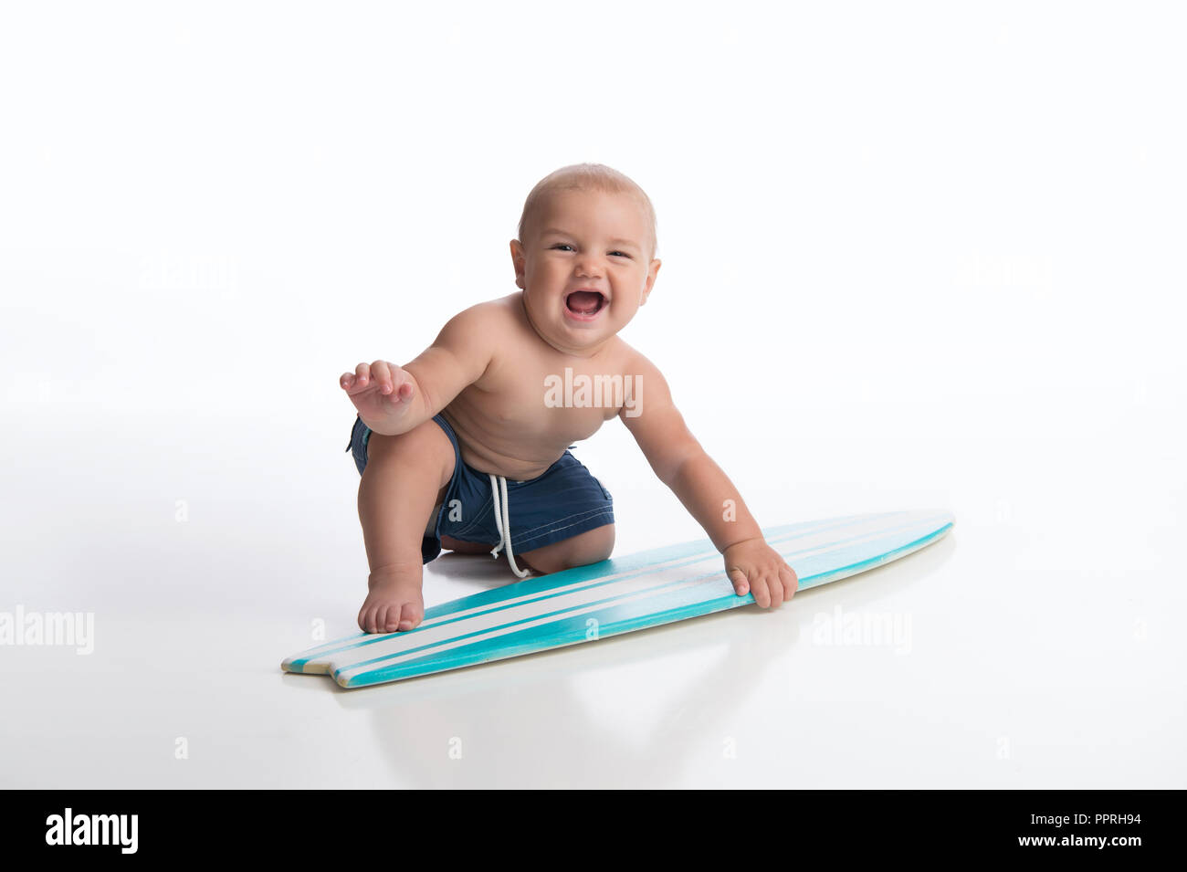 A laughing seven month old baby boy playing with a tiny surfboard. Shot in the studio on a white, seamless backdrop. Stock Photo