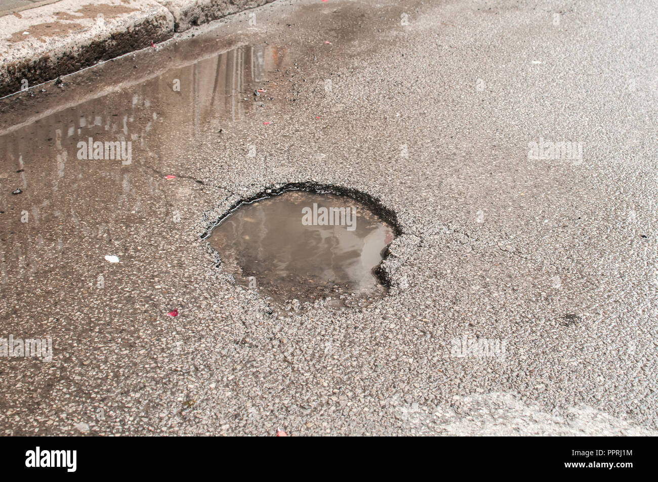 Pothole with puddle resulting from erosion of damaged road asphalt