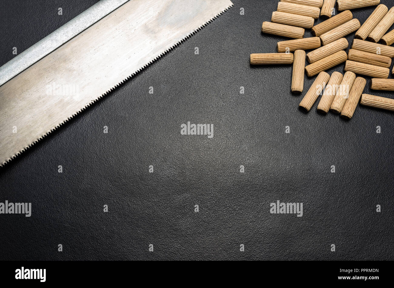 A lot of wooden pegs and hand saw for wood lying flat on a black background. Stock Photo