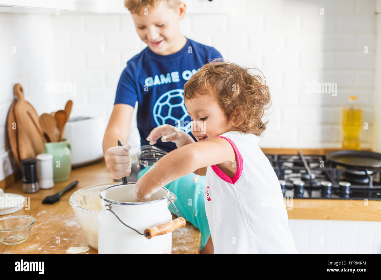 Brother and sister preparing dough for pancakes at the kitchen. Concept of food preparation, white kitchen on background. Casual lifestyle photo serie Stock Photo