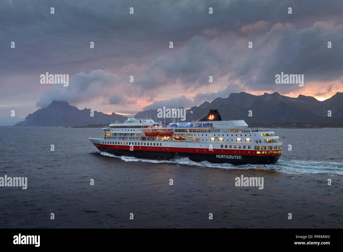 The Hurtigruten Ferry, MS FINNMARKEN, Sailing Southbound From Svolvær. The Dramatic Mountains Of The Lofoten Islands & The Midnight Sun Behind Norway. Stock Photo