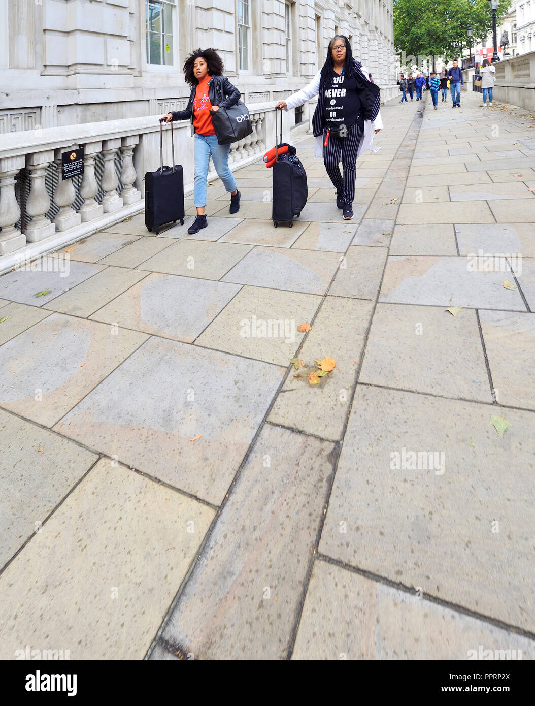 Two black women wheeling luggage in Whitehall, Westminster, London, England, UK. Stock Photo