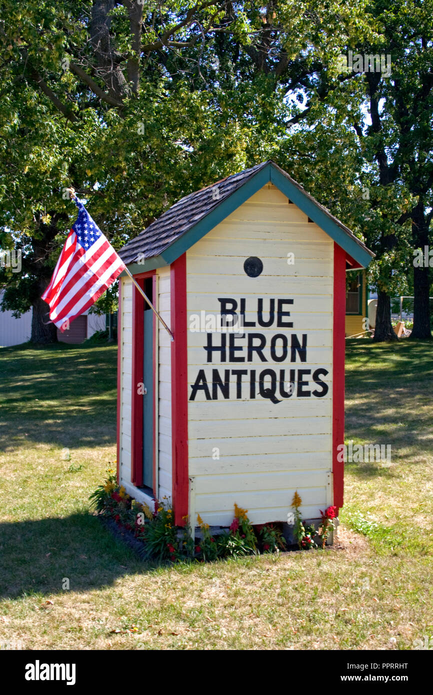 Roadside outhouse flying the American flag advertising The Blue Heron Antique shop on it's side. Vining Minnesota MN USA Stock Photo