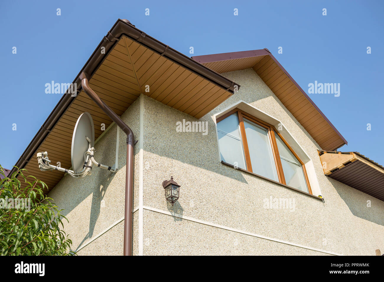 Bottom view detail of new modern house top with decorative lamp and satellite dish on stucco walls plastic attic window gutter pipe system on blue s
