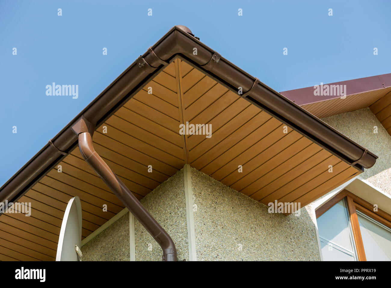 Bottom view detail of new modern house top with decorative lamp and satellite dish on stucco walls plastic attic window gutter pipe system on blue s
