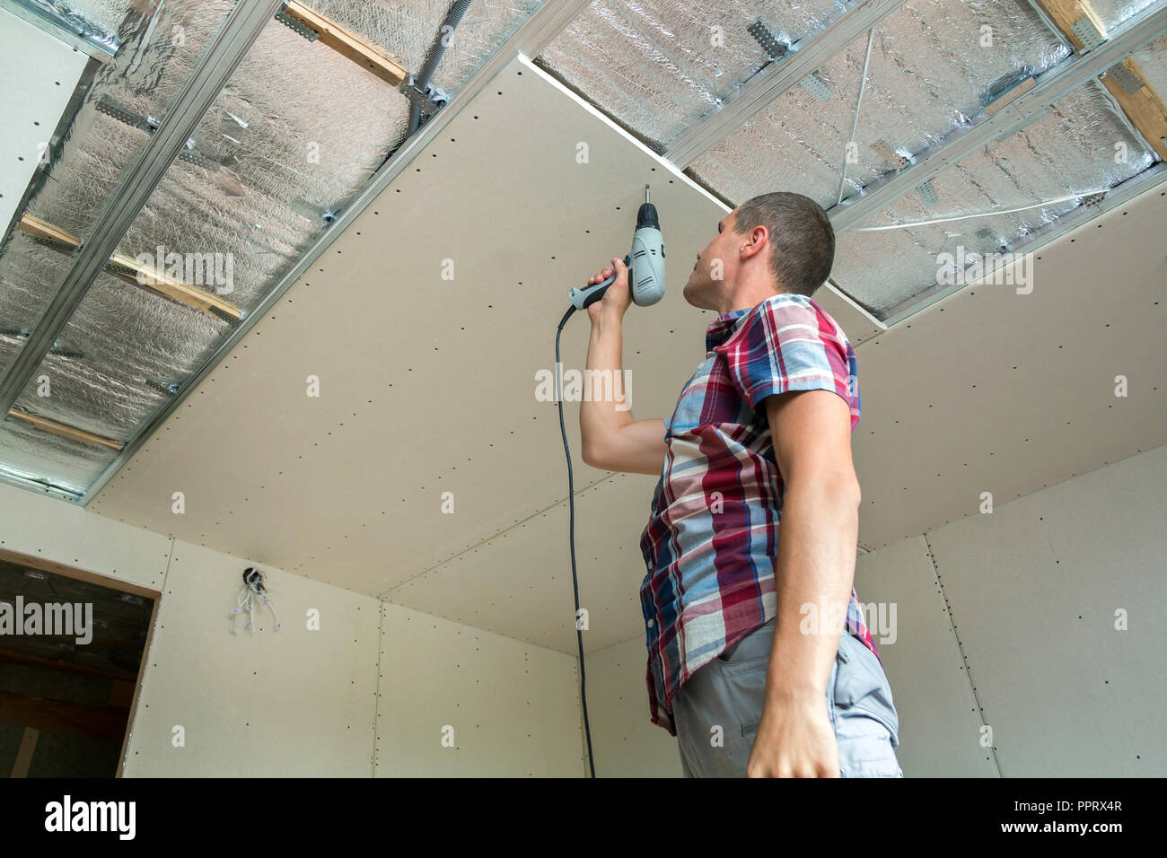 Young Man In Usual Clothing And Work Gloves Fixing Drywall Suspended Ceiling To Metal Frame Using Electrical Screwdriver On Ceiling Insulated With Shi Stock Photo Alamy