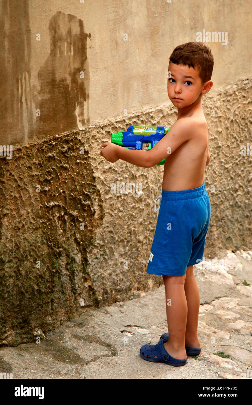 Small boy playing with his water pistol splashing the walls with water in the village of Vrbnik on the Croatian island of Krk, on the Adriatic Sea Stock Photo