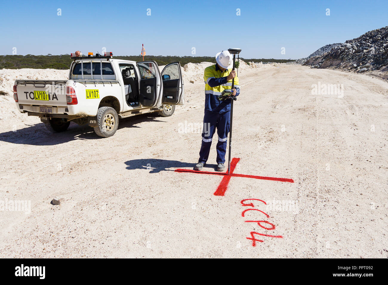 Surveyor marking reference point for use with drone to measure ore stockpile at a gold mine in Western Australia Stock Photo