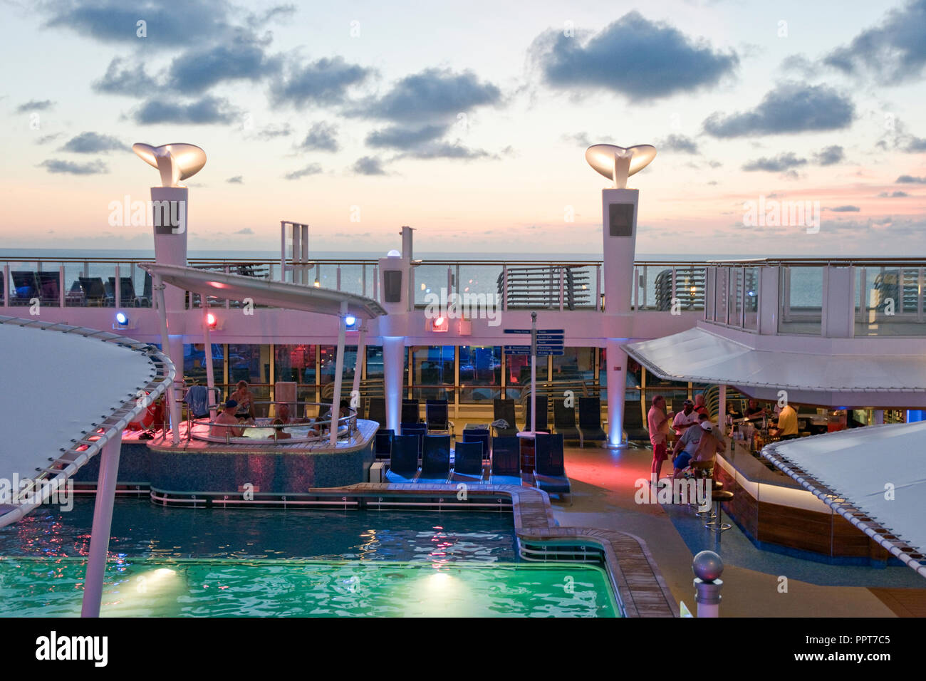 Passengers enjoy the bar and pool at sunset on the top deck of a cruise ship voyaging across the