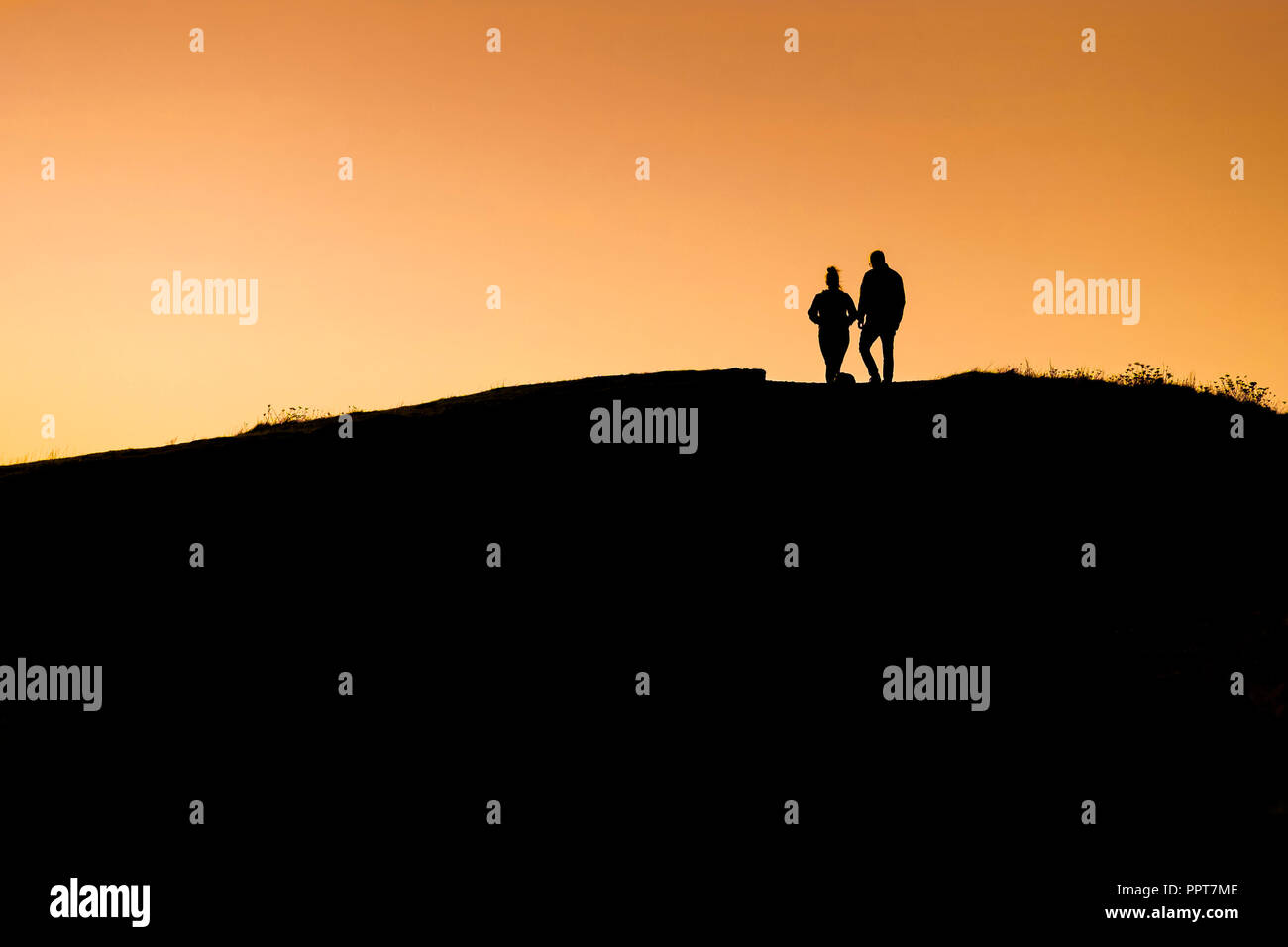 Figures seen in silhouette against an intense sunset on East Pentire in Newquay in Cornwall. Stock Photo