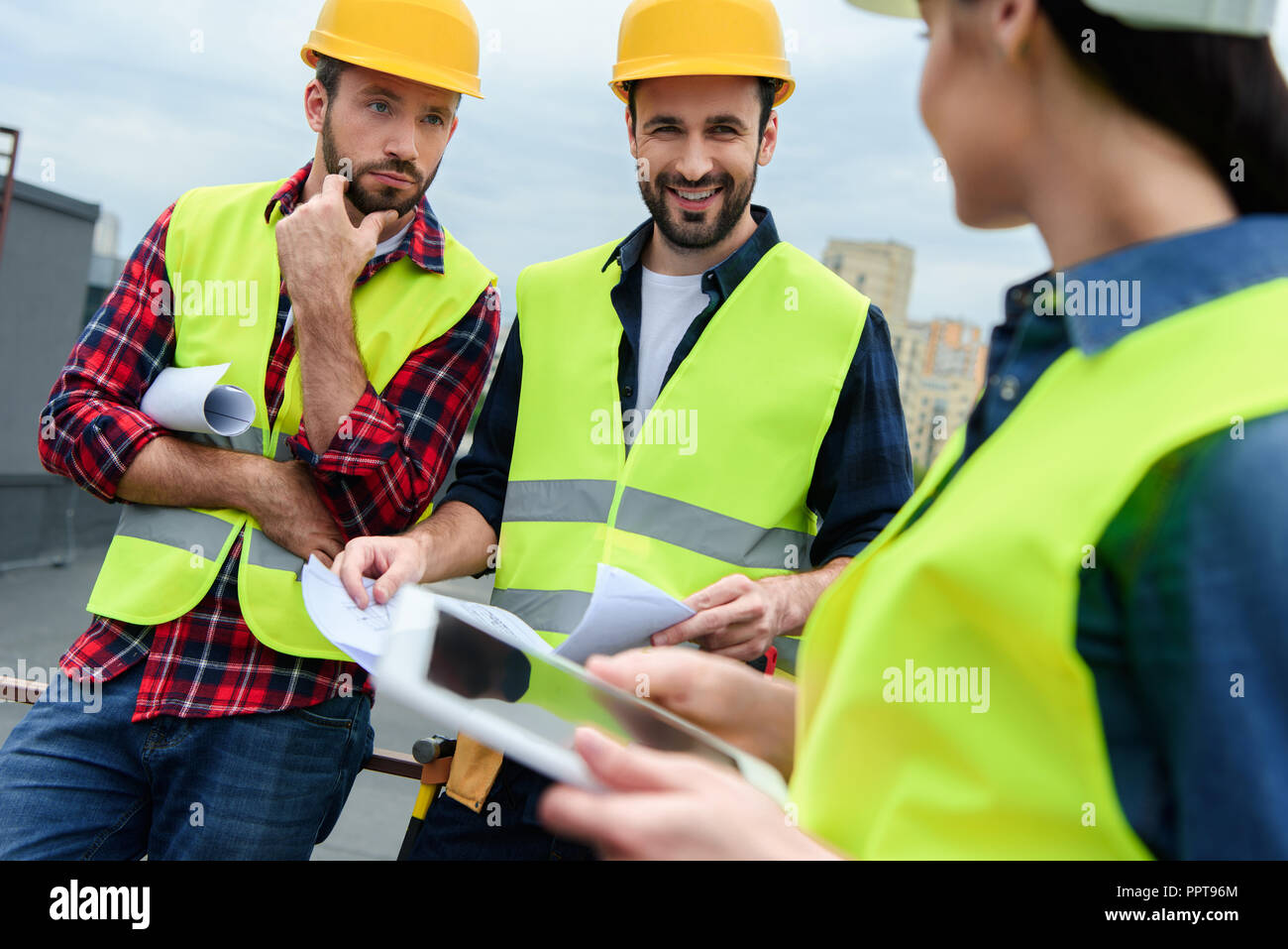 engineers in safety vests and hardhats working with digital tablet and blueprints Stock Photo