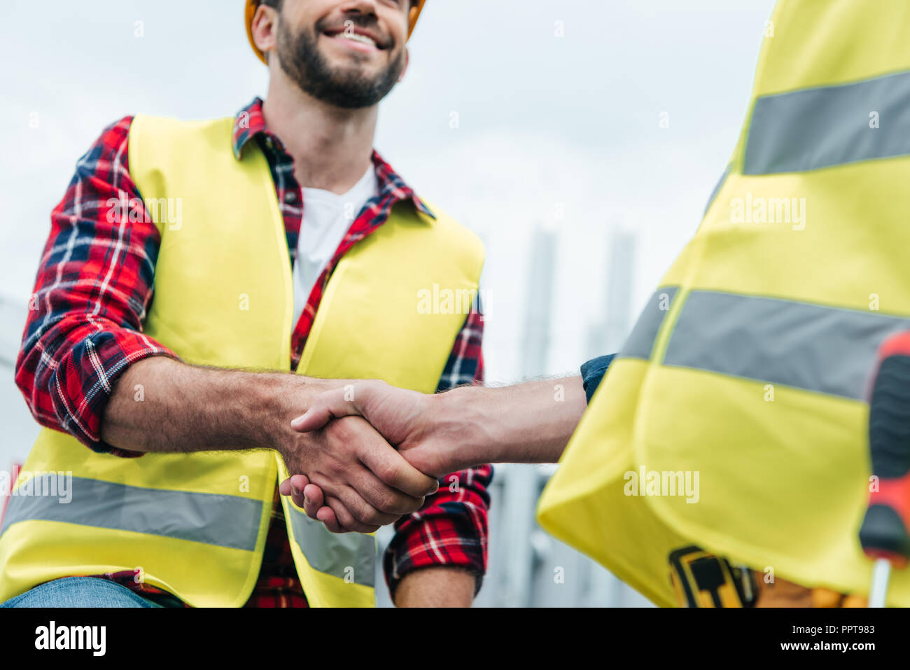 cropped view of engineers in safety vests shaking hands on roof Stock Photo