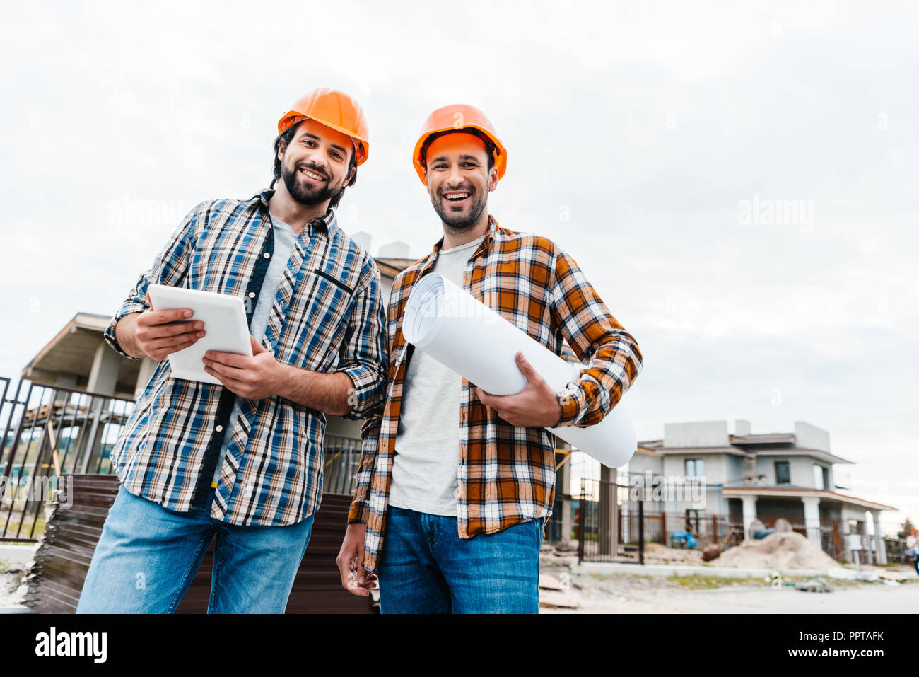 architects with blueprint and tablet looking at camera at construction ...