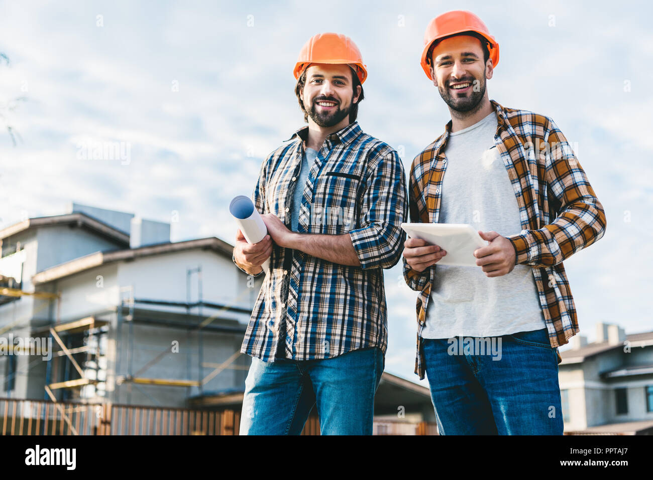 architects with blueprint and tablet looking at camera at construction ...