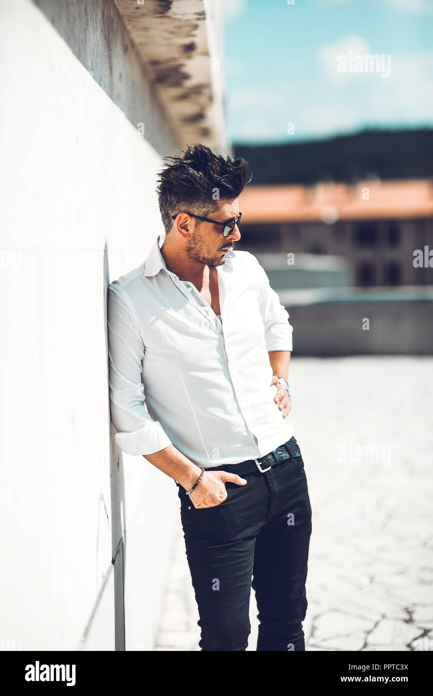 Portrait of a successful young businessman dressed leaning to wall . Concept Fashionable Young Man Stock Photo