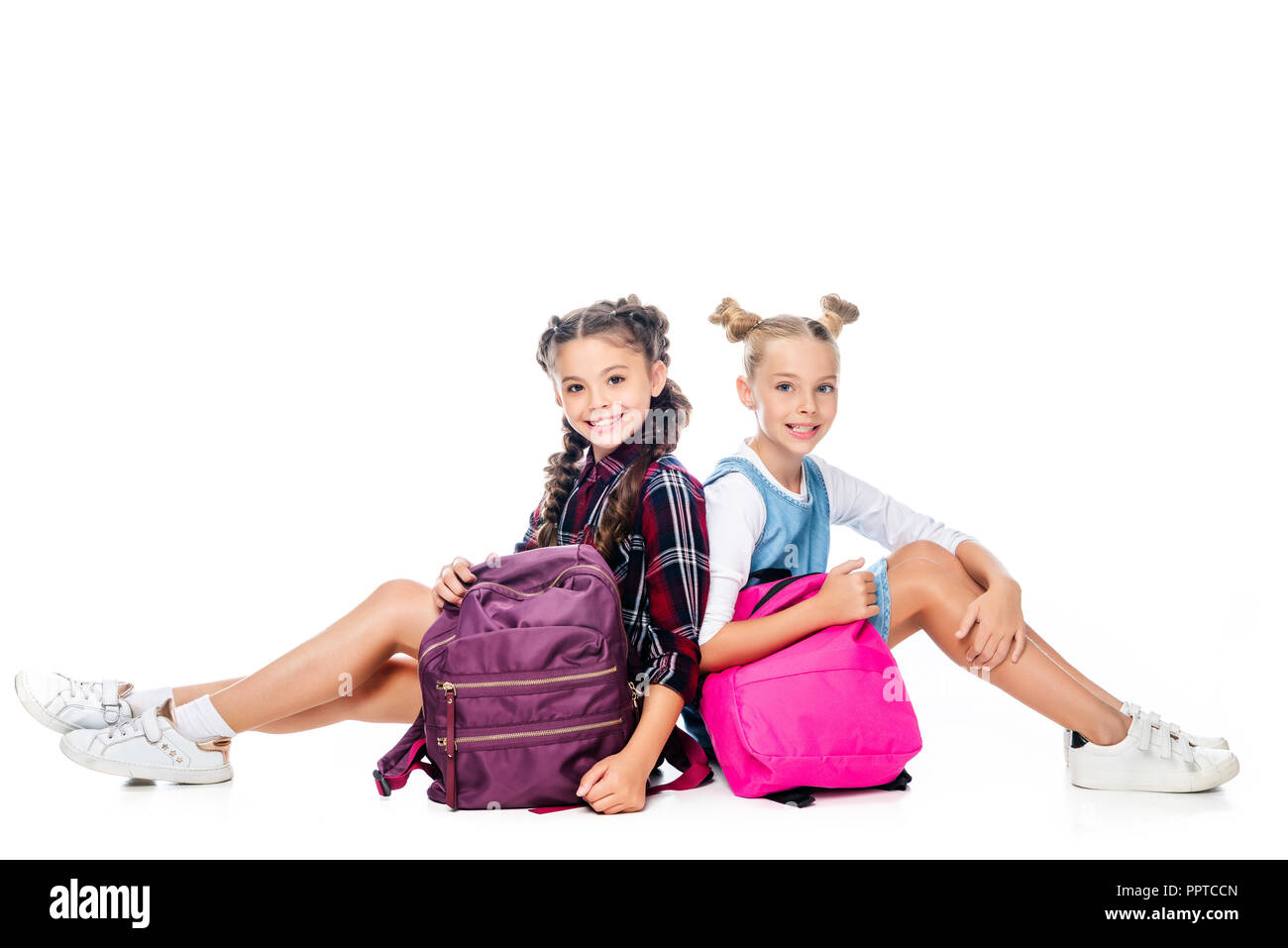 schoolchildren sitting with backpacks and looking at camera isolated on white Stock Photo