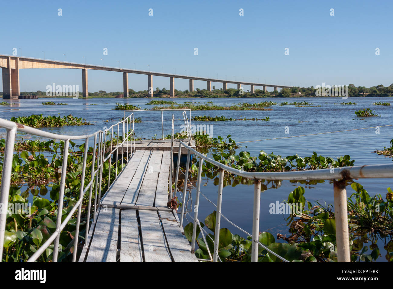 Rustic wooden footpath bridge over water, small dock pier, Rio (River) Paraguay, Puente (Bridge) Remanso Castillo on the background, M.R.A., Paraguay Stock Photo