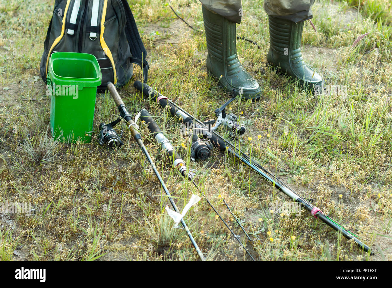 Fishing rods are lying on the ground. An angler in rubber boots